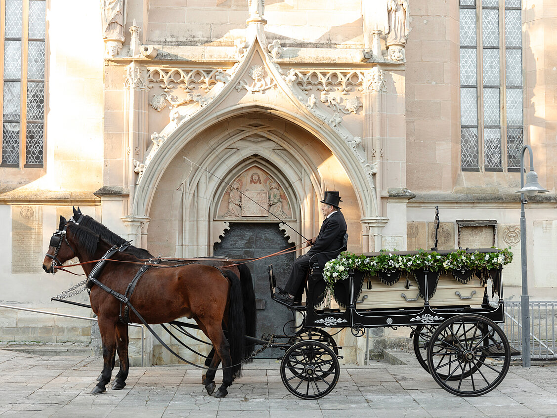 Eine Bestattungskutsche von Eiberger & Krauß in Schwarz und Silber transportiert einen Sarg von einer Trauerfeier.