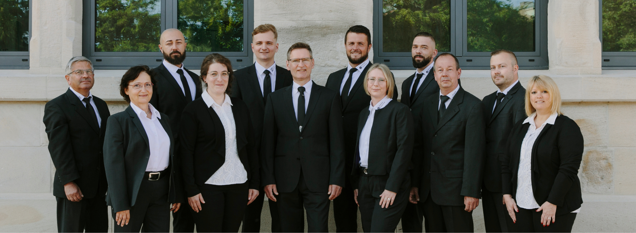 Team von Krauß Bestattungen in Aalen, professionell gekleidet in schwarzen Anzügen, posierend in einer grünen, friedlichen Umgebung vor einer historischen Kapelle.