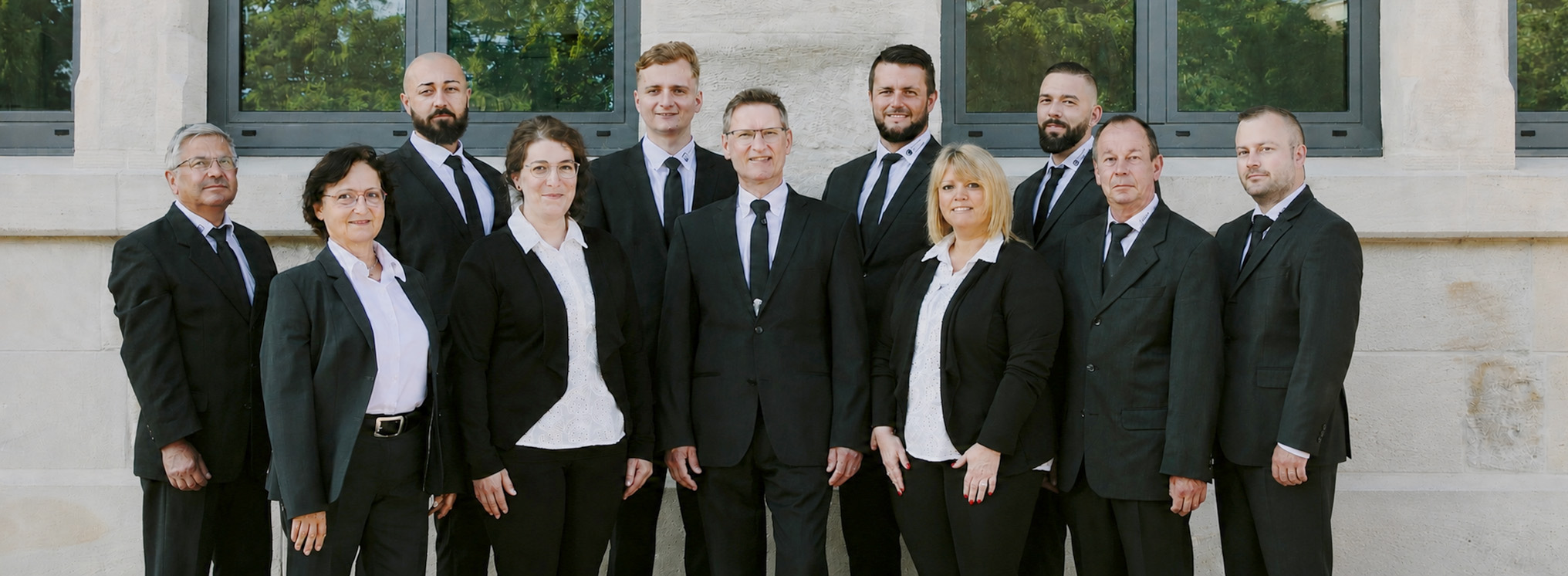 Team von Krauß Bestattungen in Aalen, professionell gekleidet in schwarzen Anzügen, posierend in einer grünen, friedlichen Umgebung vor einer historischen Kapelle.