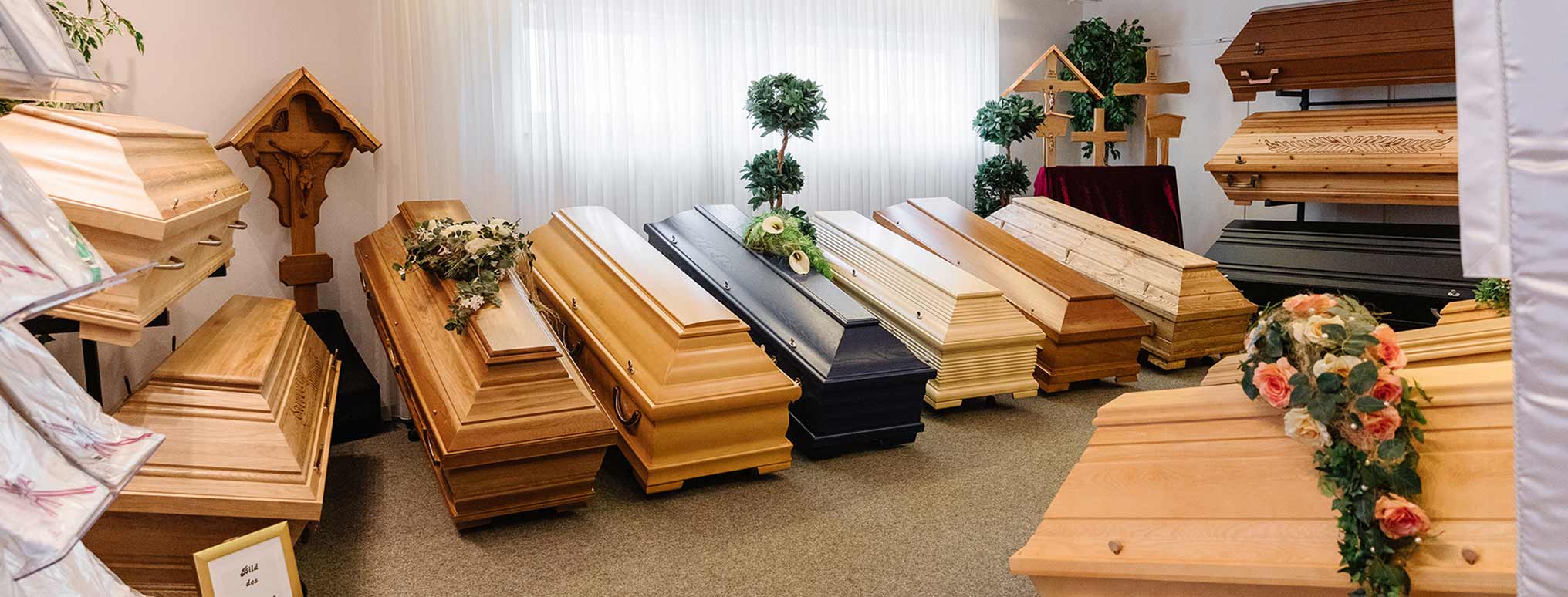 Sargausstellung mit einer Auswahl an Holzsärgen in verschiedenen Designs, geschmückt mit Blumen und religiösen Symbolen.